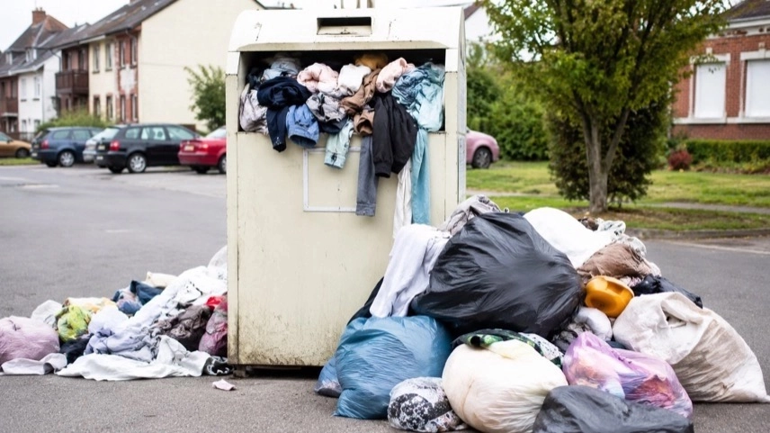 Überfüllter Altkleidercontainer mit Müllsäcken und Alttextilien auf einem Parkplatz im Oberharz
